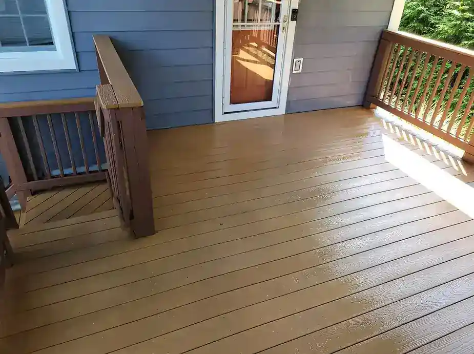 Composite deck with wood railing, washed and shining beside blue siding